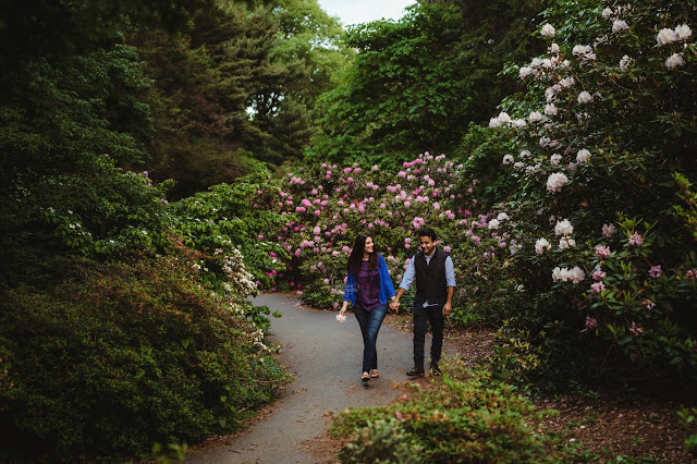 Engaged couple walking through Highland park hand in hand looking at each other happily surrounded by flowers