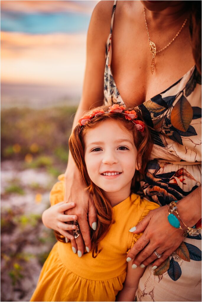 Clearwater Beach, FL Family Photography. Mother and daughter lovingly embrace at sunset on the sand dunes at Clearwater beach during golden hour full of radiant sunset colors